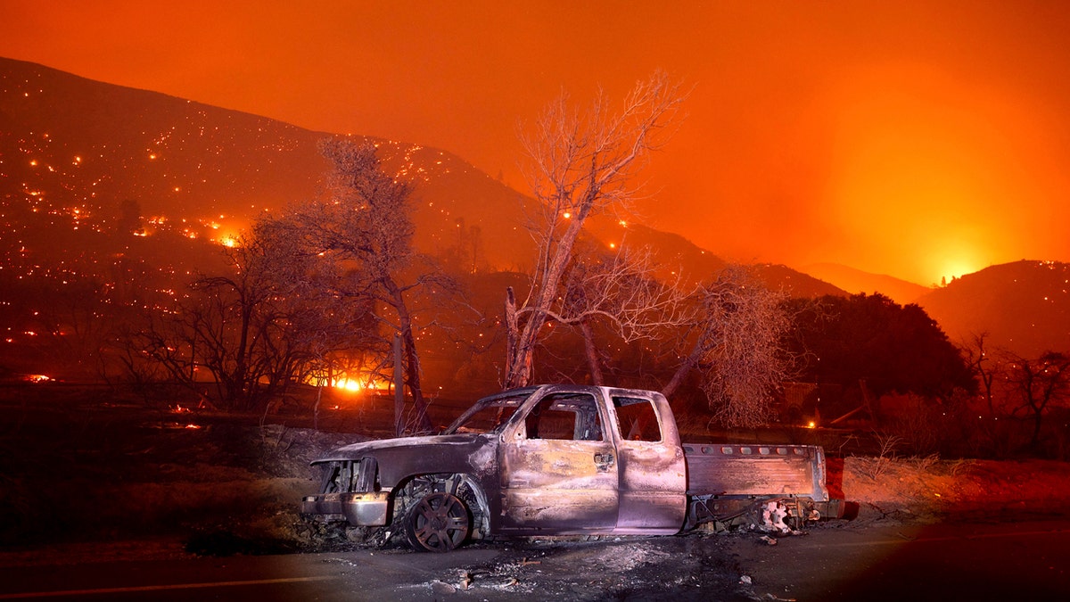 A scorched vehicle rests on Pine Canyon Rd. as the Lake Fire burns a hillside in the Angeles National Forest, Calif., north of Santa Clarita on Thursday, Aug. 13, 2020.