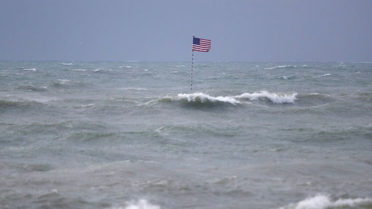 An American flag flies from the shipwreck of the Breconshire, as waves churned up by Tropical Storm Isaias crash around it, Sunday, Aug. 2, 2020, in Vero Beach, Fla.