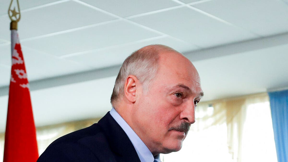 Belarusian President Alexander Lukashenko walks after voting at a polling station with a Belarusian national flag on the left, during the presidential election in Minsk, Belarus, Sunday, Aug. 9, 2020. (AP Photo/Sergei Grits)