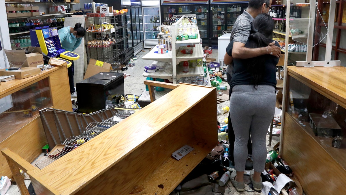 Yogi Dalal hugs his daughter Jigisha as his other daughter Kajal, left, bows her head at the family food and liquor store Monday, Aug. 10, 2020, after the family business was vandalized in Chicago. (AP Photo/Charles Rex Arbogast)