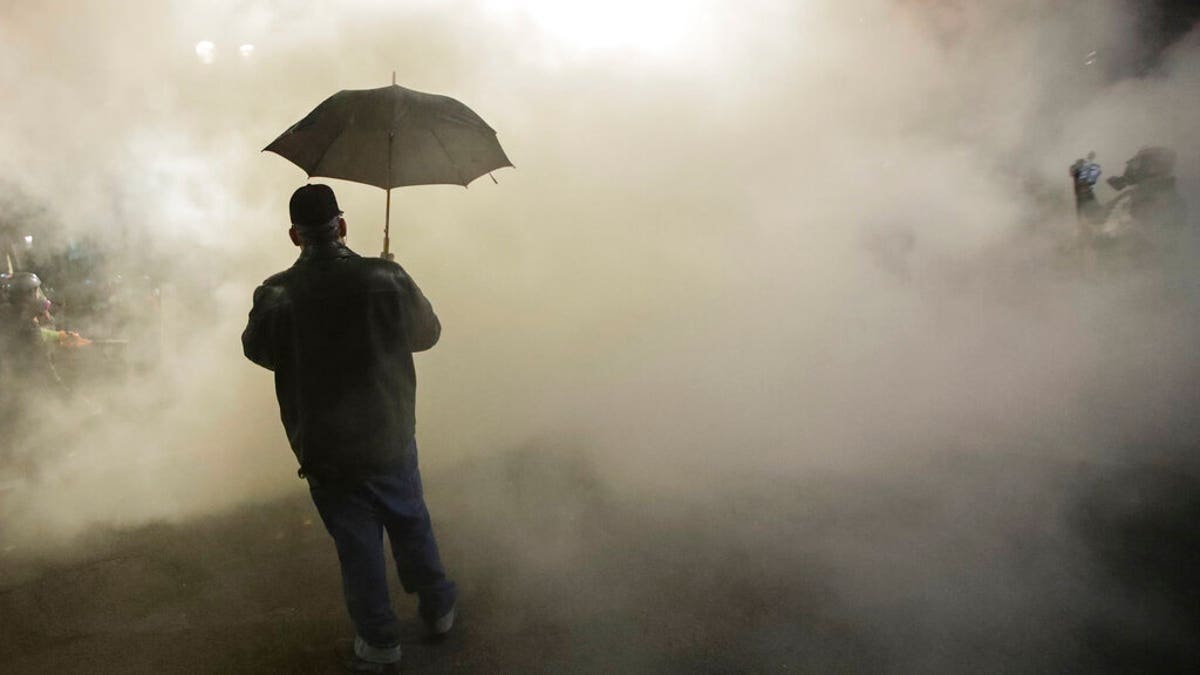 In this July 25, 2020, file photo, a protester carries an umbrella as federal officers deploy tear gas during a protest. (AP Photo/Marcio Jose Sanchez, File)