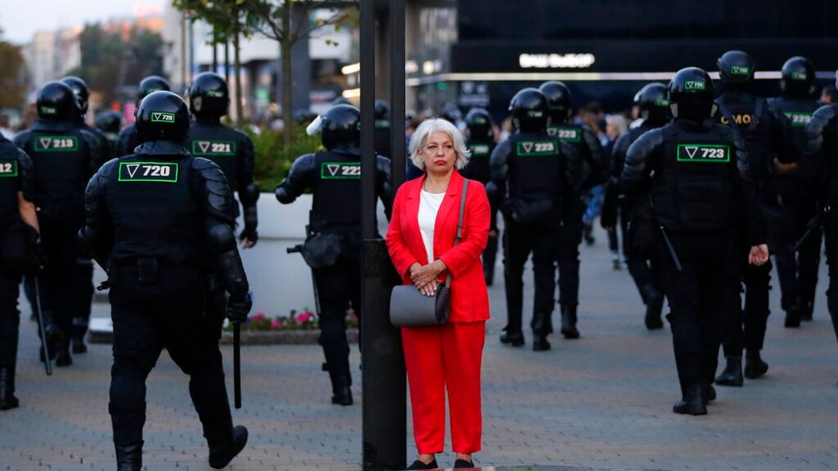 A woman stands in a street as police gather to block protesters during a mass protest following presidential elections in Minsk, Belarus, Monday, Aug. 10, 2020. 