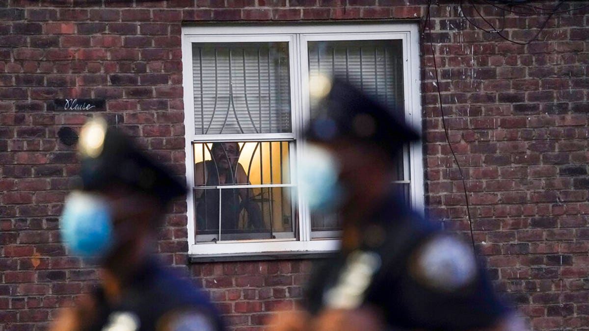 A neighbor watches New York City Police Department officers work a crime scene where several young men were shot and wounded at the Ravenswood Houses, on Aug. 18, 2020, in Queens, New York. (AP Photo/John Minchillo)