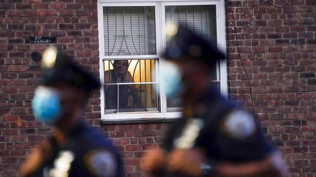 A neighbor watches New York City Police Department officers work a crime scene where several young men were shot and wounded at the Ravenswood Houses, on Aug. 18, 2020, in Queens, New York. (AP Photo/John Minchillo)