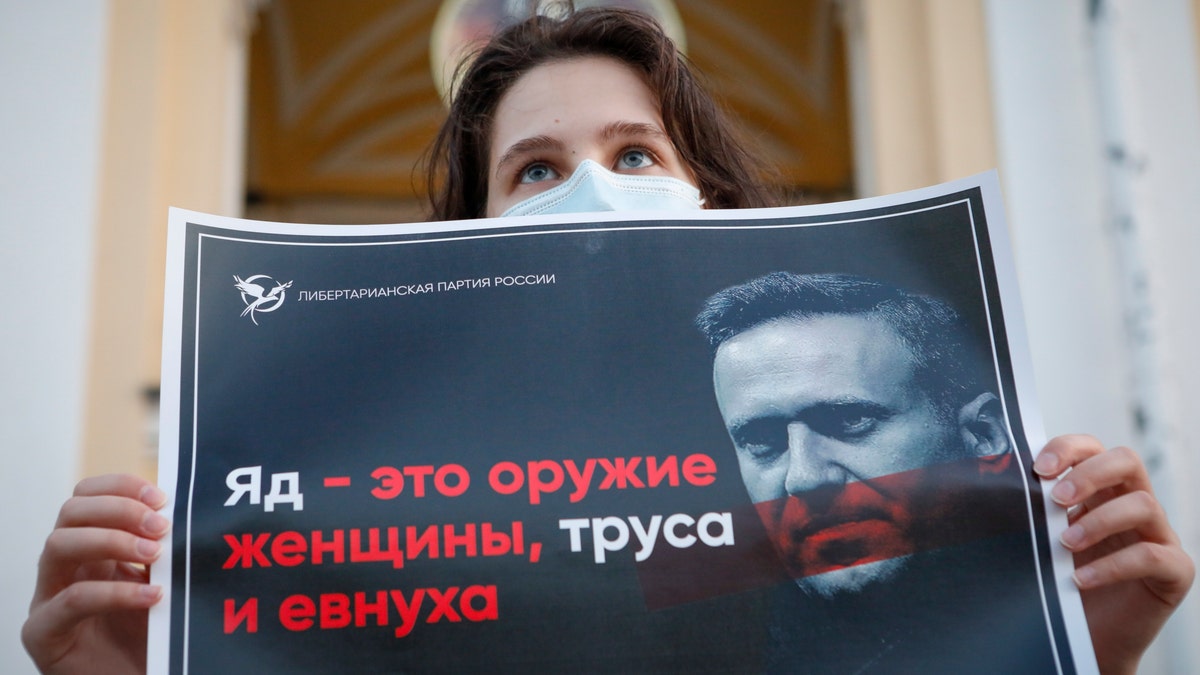 A protester stands holds a poster reads "poison is the weapon of a woman, a coward and a eunuch!" during a picket in support of Russian opposition leader Alexei Navalny in the center of St. Petersburg, Russia, Thursday, Aug. 20, 2020. (AP Photo/Elena Ignatyeva)