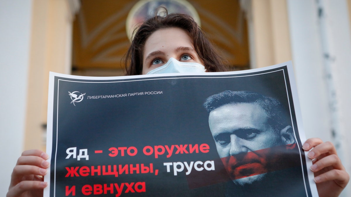 A protester stands holds a poster reads "poison is the weapon of a woman, a coward and a eunuch!" during a picket in support of Russian opposition leader Alexei Navalny in the center of St. Petersburg, Russia, Thursday, Aug. 20, 2020. (AP Photo/Elena Ignatyeva)