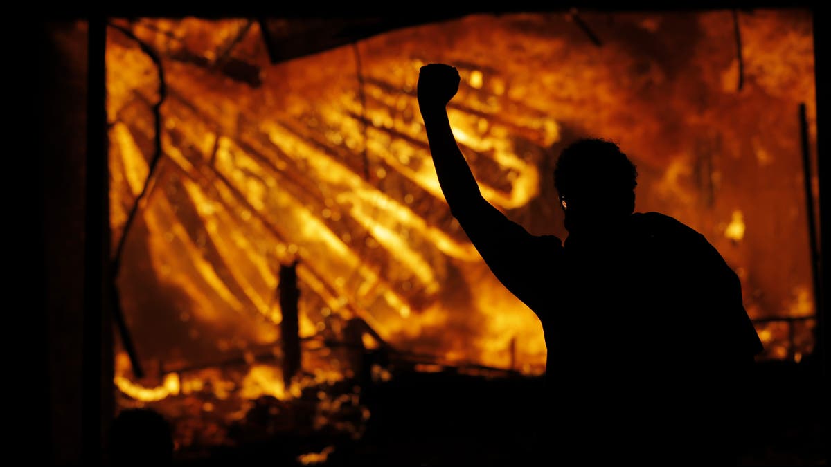 In this May 28, 2020 file photo, a protester gestures in front of the burning 3rd Precinct building of the Minneapolis Police Department in Minneapolis. (AP Photo/Julio Cortez File)