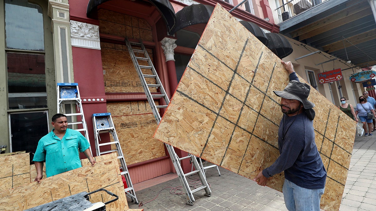 Cesar Reyes, right, carries a sheet of plywood to cut to size as he and Robert Aparicio, left, install window coverings at Strand Brass and Christmas on the Strand, 2115 Strand St., in Galveston on Monday, Aug. 24, 2020. ( Jennifer Reynolds/The Galveston County Daily News via AP)
