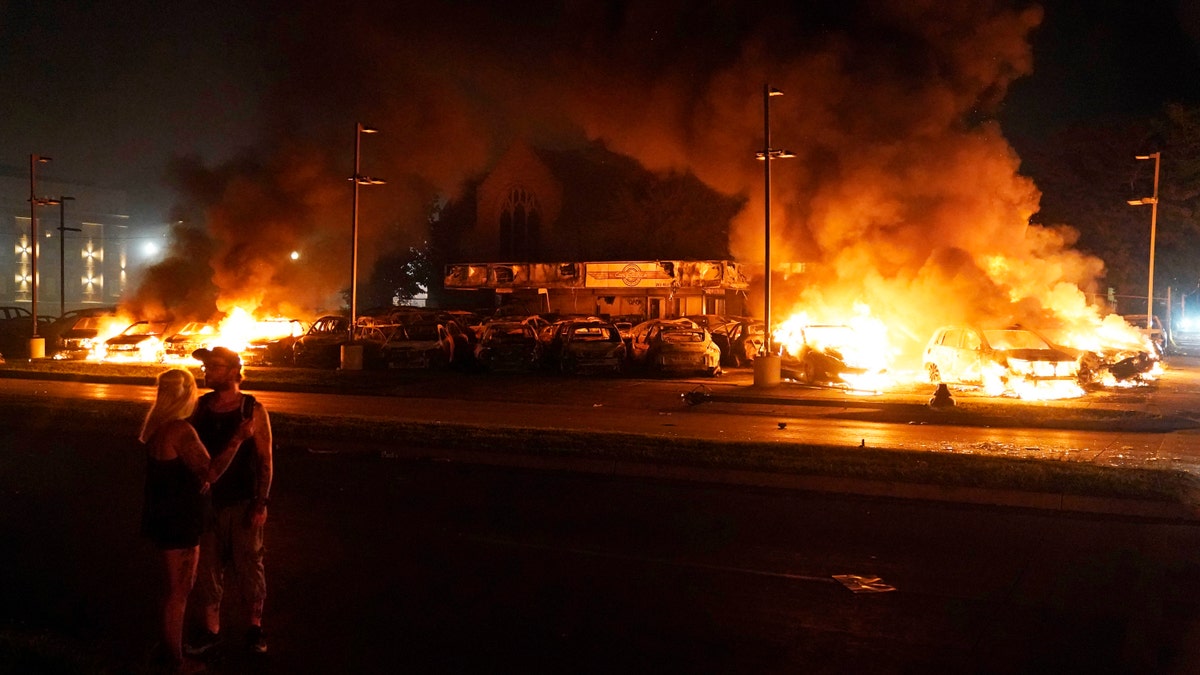 Bystanders look on as cars burn after protesters set fire to a used auto lot late Monday, Aug. 24, 2020, in Kenosha, Wis. (AP Photo/David Goldman)