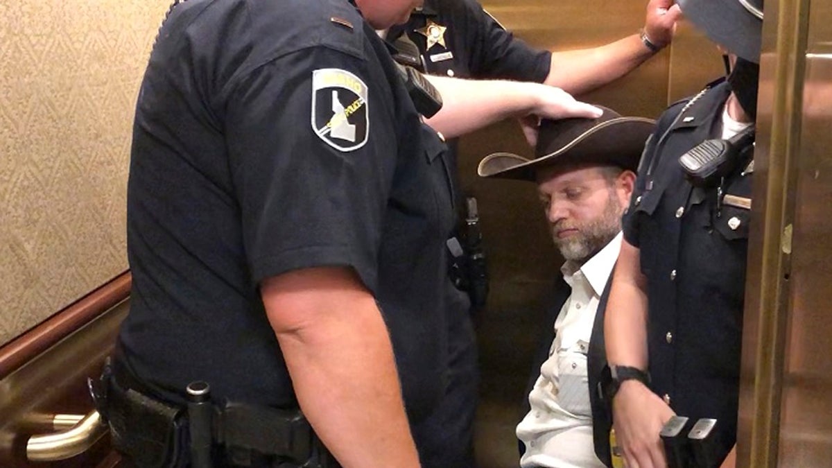 This image taken from video shows anti-government activist Ammon Bundy, rear, being wheeled into an elevator in a chair following his arrest at the Idaho Statehouse in Boise, Idaho on Tuesday. Authorities arrested Bundy after he refused to leave a meeting room where a few hours earlier angry protesters forced out lawmakers. (AP Photo/Keith Ridler)