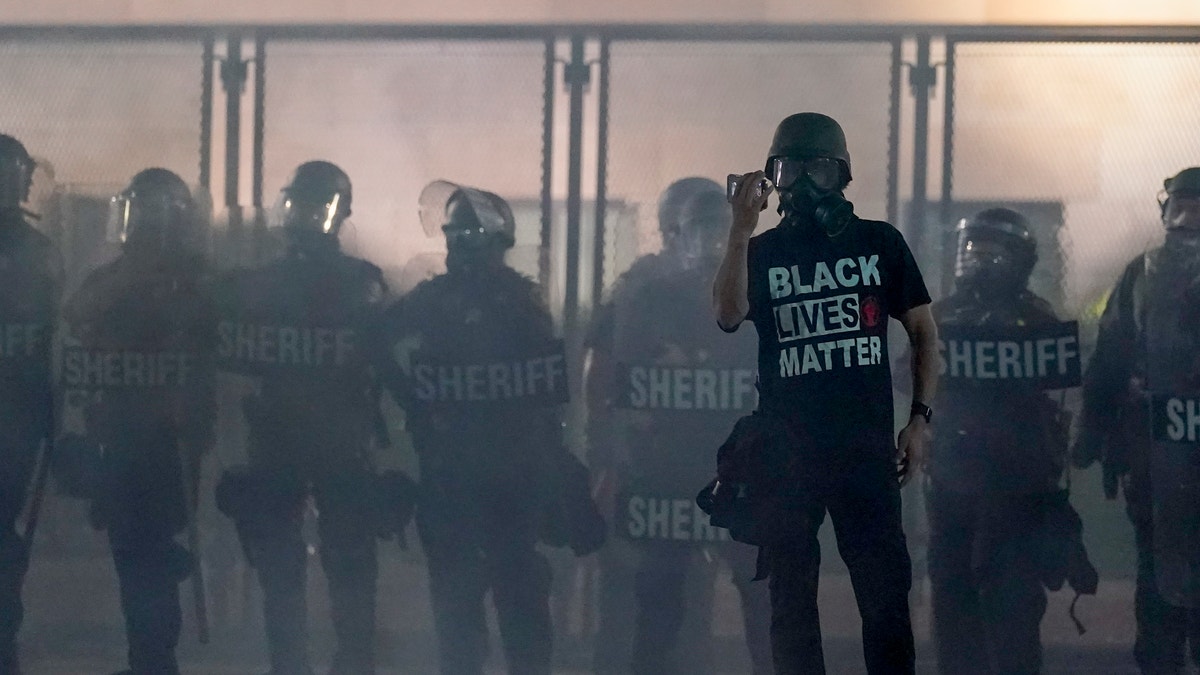 A protester holds up a phone as he stands in front of authorities in Kenosha, Wis. (AP Photo/Morry Gash, File)