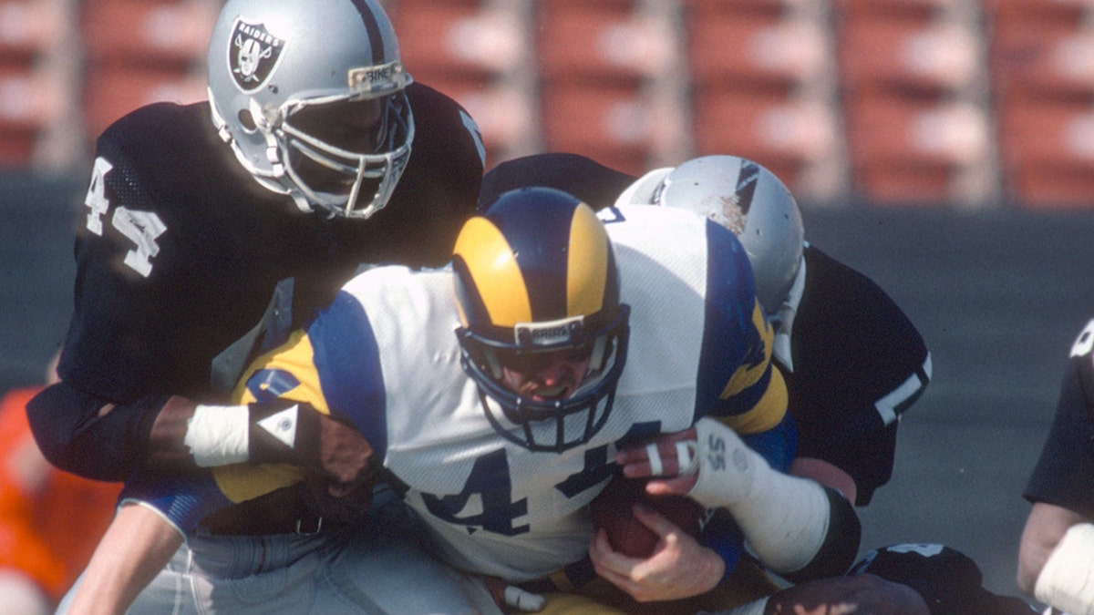 Mike Guman #44 of the Los Angeles Rams gets tackled by Howie Long #75 and Burgess Owens #44 of the Los Angeles Raiders during an NFL football game, Dec. 18, 1982. (Focus on Sport/Getty Images)