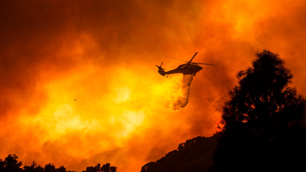 In this Aug. 12, 2020, file photo, a helicopter drops water on the Lake Hughes Fire in Angeles National Forest north of Santa Clarita, Calif.
