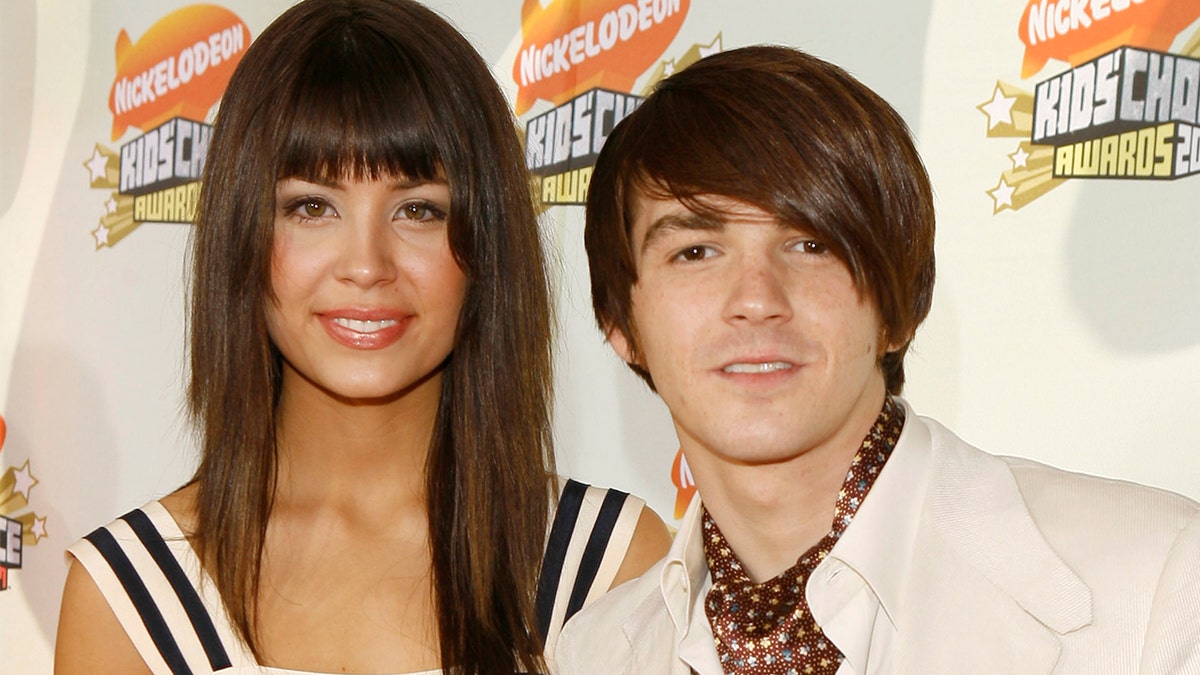 Melissa Lingafelt smiles in a white dress with blue stripes next to boyfriend Drake Bell in a white suit