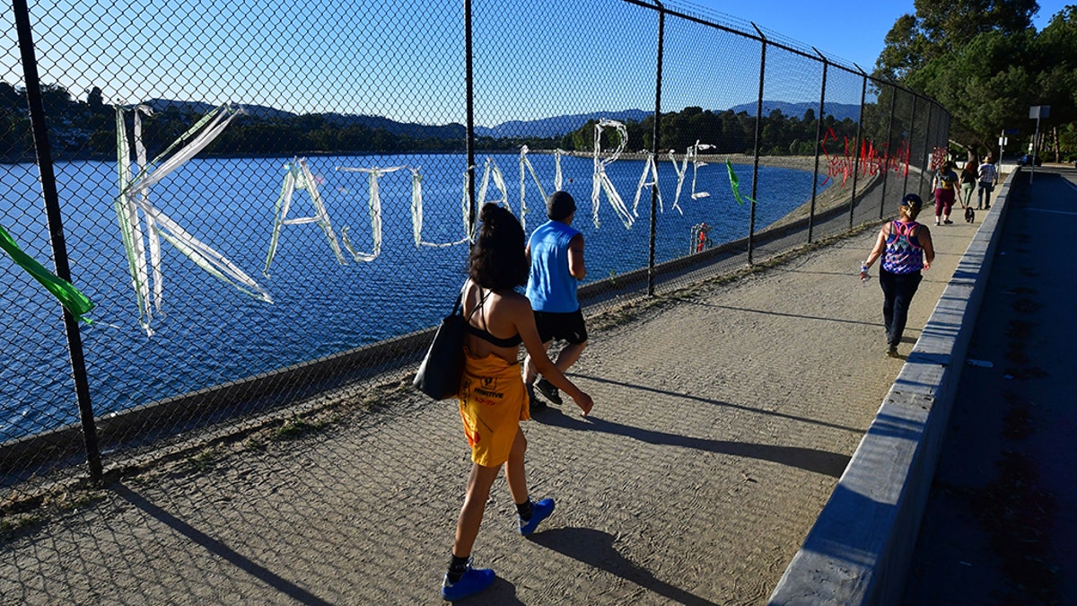 People walk past a chain-link fence surrounding Silver Lake Reservoir in Los Angeles, where an art installation protesting police brutality spells out, in colourful woven fabric, the names of unarmed African Americans who have been killed by police. 