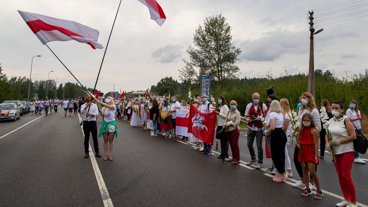 Supporters of Belarus opposition from Lithuania hold and wave historical Belarusian flags during the "Freedom Way", a human chain of about 50,000 strong from Vilnius to the Belarusian border, near Medininkai, Lithuanian-Belarusian border crossing east of Vilnius, Lithuania, Sunday, Aug. 23, 2020. In Aug. 23, 1989, around 2 million Lithuanians, Latvians, and Estonians joined forces in a living 600 km (375 mile) long human chain Baltic Way, thus demonstrating their desire to be free. Now, Lithuania is expressing solidarity with the people of Belarus, who are fighting for freedom today. (AP Photo/Mindaugas Kulbis)