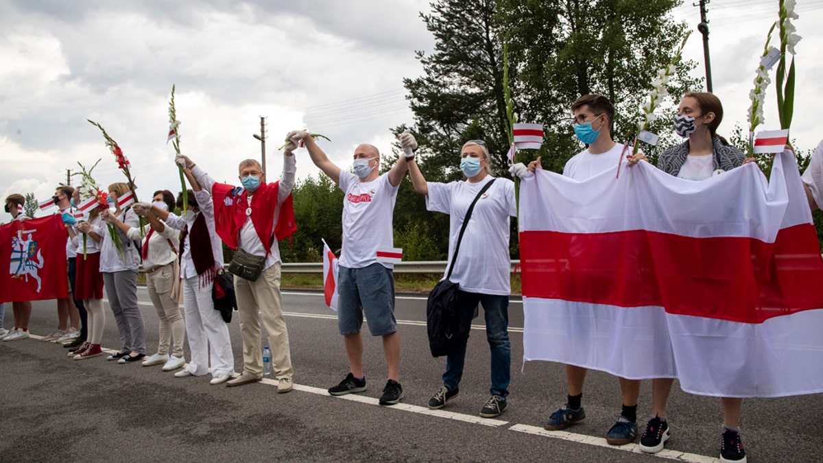 People hold hands, historical white-red-white flags of Belarus and flowers as they participate in a "Freedom Way", a human chain of about 50,000 strong from Vilnius to the Belarusian border, during a protest near Medininkai, Lithuanian-Belarusian border crossing east of Vilnius, Lithuania, Sunday, Aug. 23, 2020. In Aug. 23, 1989, around 2 million Lithuanians, Latvians, and Estonians joined forces in a living 600 km (375 mile) long human chain Baltic Way, thus demonstrating their desire to be free. Now, Lithuania is expressing solidarity with the people of Belarus, who are fighting for freedom today. (AP Photo/Mindaugas Kulbis)