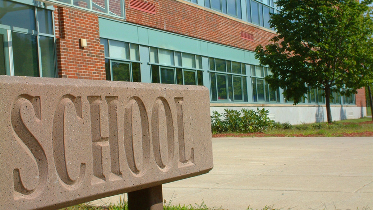 Brown school sign in front of a brick and teal building during daytime