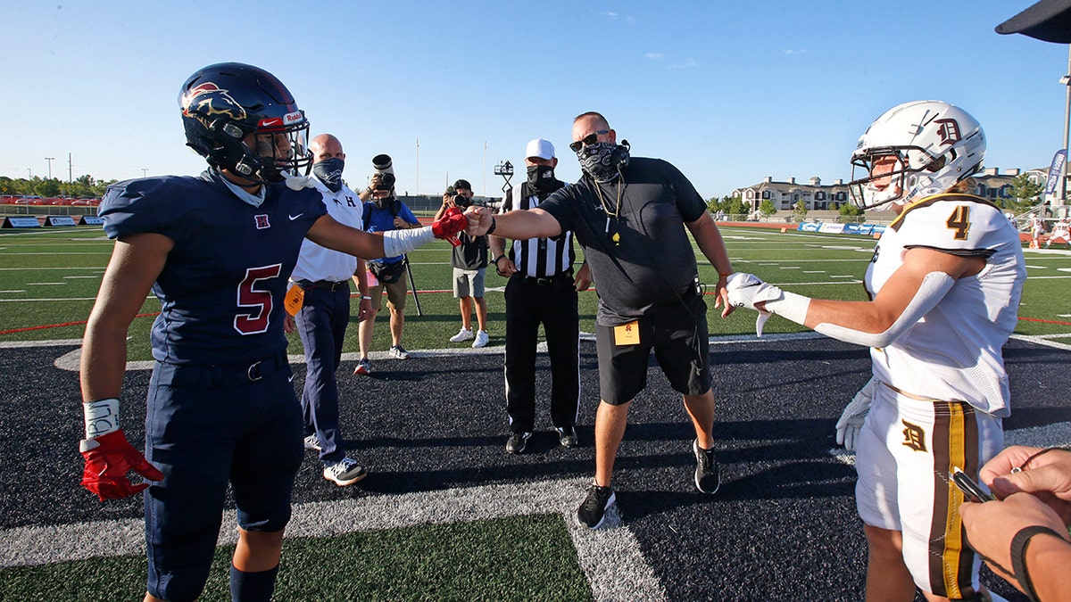 Davis High head coach Mitch Arquette, center, fist bumps Herriman High's Brock Hollingsworth (5) during the coin toss before the start of a high school football game on Thursday, Aug. 13, 2020, in Herriman, Utah. Utah is among the states going forward with high school football this fall. (AP Photo/Rick Bowmer)