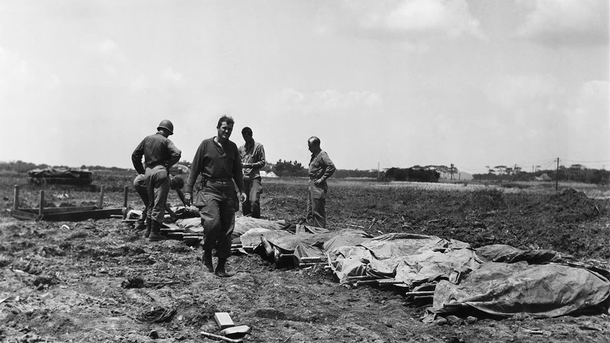 FILE - In this B/W file photo dated May 9, 1945, while American cities were going wild on an unconfirmed report of Germany's unconditional surrender, American soldiers and marines are checking the identification of their dead on May 9, 1945, on Okinawa, Japan. Resistance continues to be savage on this island in Japan's front yard. Following the defeat of the Nazis on May 8, 1945, Allied troops carried on fighting until Japan’s surrender, but many of them felt their efforts had not been fully recognized and dubbed themselves the “forgotten army.”(AP Photo/Sam Goldstein, FILE)
