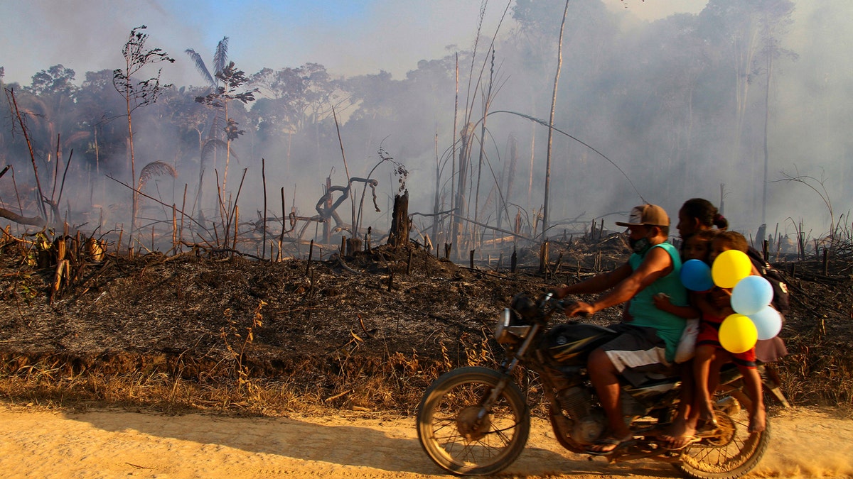 A family rides along a paved dirt road in an area scorched by fires near Labrea, Amazonas state, Brazil, Friday, Aug. 7, 2020.