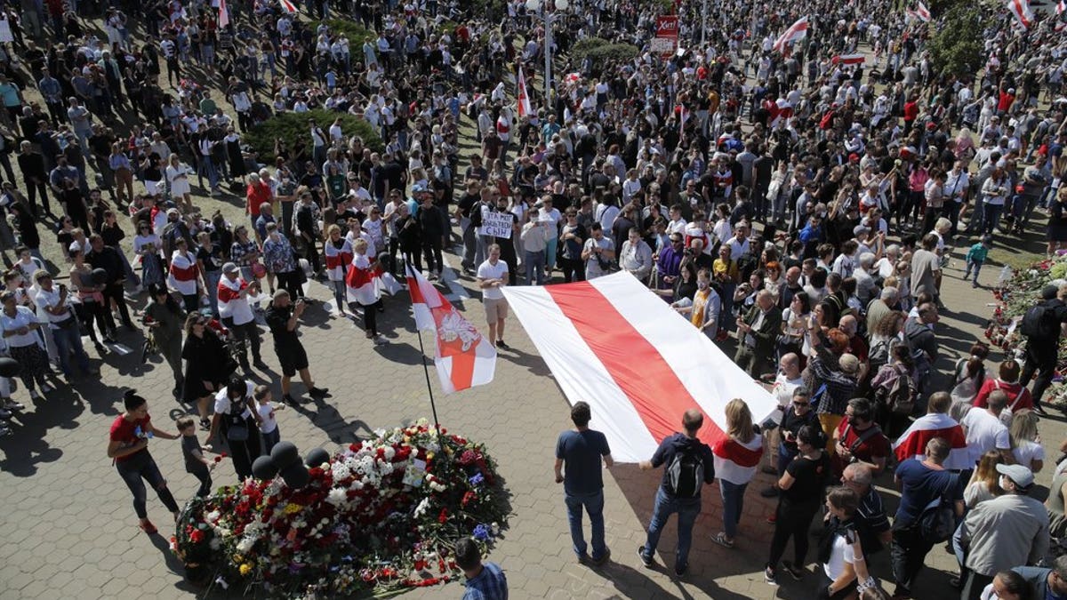People hold an old Belarusian National flag and gather at the place where Alexander Taraikovsky died amid the clashes protesting the election results, during his civil funeral in Minsk, Belarus, Saturday, Aug. 15, 2020. Taraikovsky died Monday as demonstrators roiled the streets of the capital Minsk, denouncing official figures showing that authoritarian President Alexander Lukashenko, in power since 1994, had won a sixth term in office. (AP Photo/Dmitri Lovetsky)