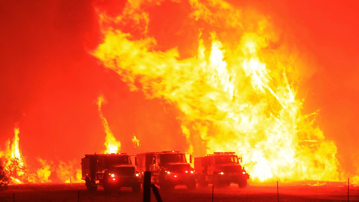 Firefighters take refuge in their trucks in a cleared field as a wildfire also known as the Hennessey Fire jumped Knoxville Berryessa Road, west of Sacramento, Calif., Tuesday, Aug. 18, 2020.