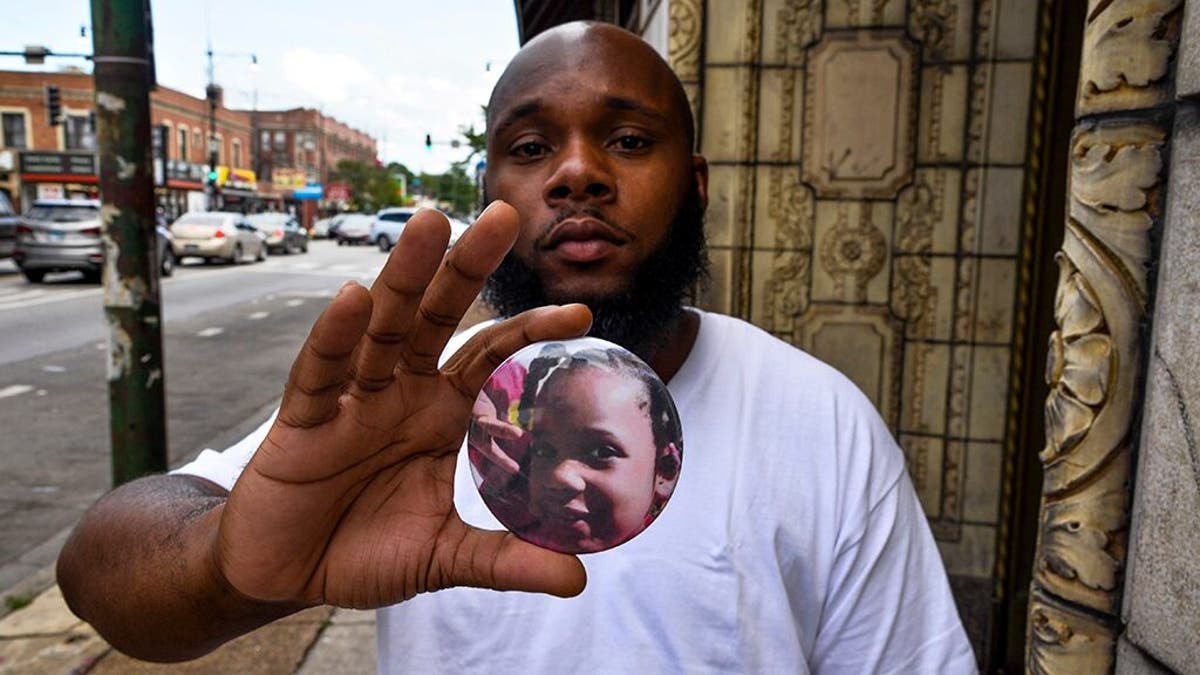 Nathan Wallace stands outside of his home holding a button showing his daughter, Natalia Wallace. Natalia, 7, was killed on the west side of Chicago on July 4. (AP Photo/Matt Marton)