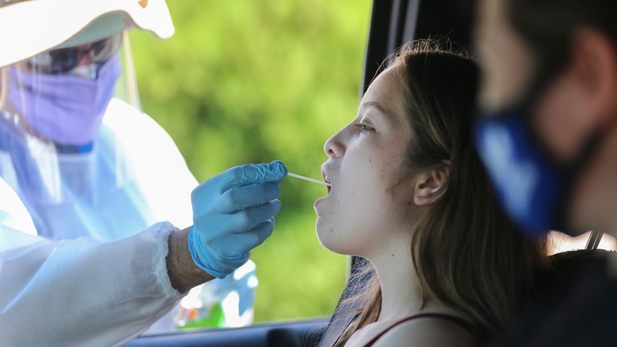 A health care worker gives a girl a throat swab test at a drive-in coronavirus (COVID-19) testing center at M.T.O. Shahmaghsoudi School of Islamic Sufism on Aug. 11, 2020, in Los Angeles, California. (Mario Tama/Getty Images)