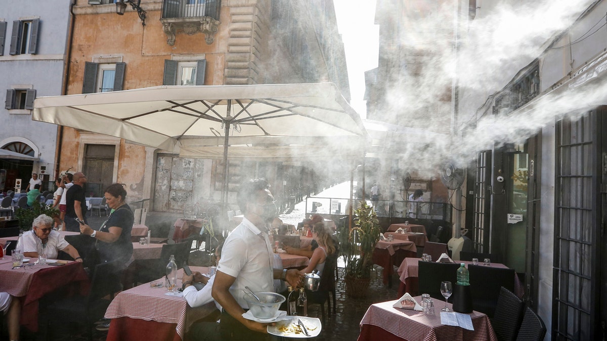 A fan sprays water as customers sit outside a cafe in downtown Rome, Friday, July 31, 2020.