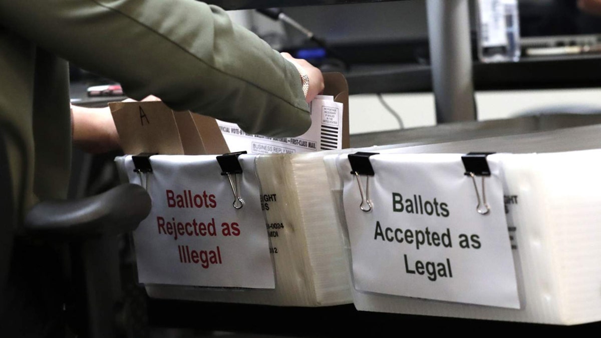 A Miami-Dade County Elections Department employee places a vote-by-mail ballot for the August 18 primary election into a box for rejected ballots as the canvassing board meets at the Miami-Dade County Elections Department, Thursday, July 30, 2020, in Doral, Fla. (AP Photo/Lynne Sladky)