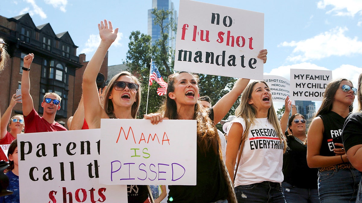 Maria Harvey and her sister Ashley Makridakis hold up signs during a protest against mandatory flu vaccinations, outside the Massachusetts State House, Sunday, Aug. 30, 2020, in Boston. Public health authorities say flu shots are very important this year to avoid overburdening the health system. amid the coronavirus pandemic. (Nancy Lane/Boston Herald via AP)