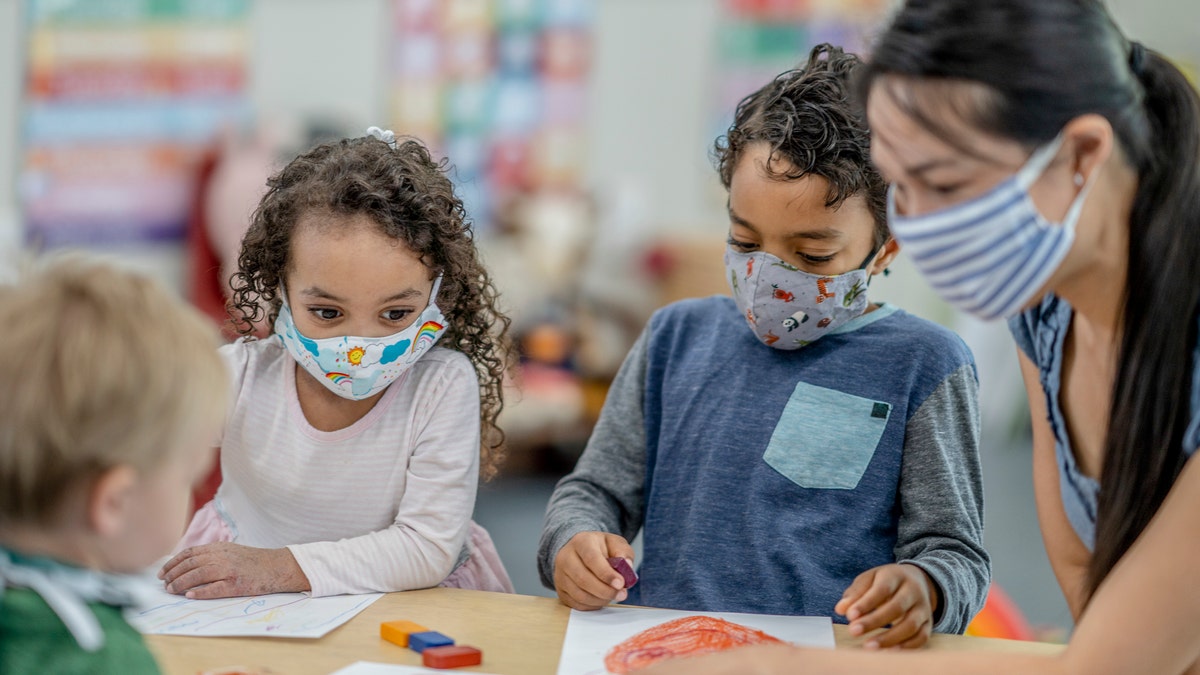 Multi-ethnic group of children coloring at a table while wearing protective face masks to avoid the transfer of germs. 