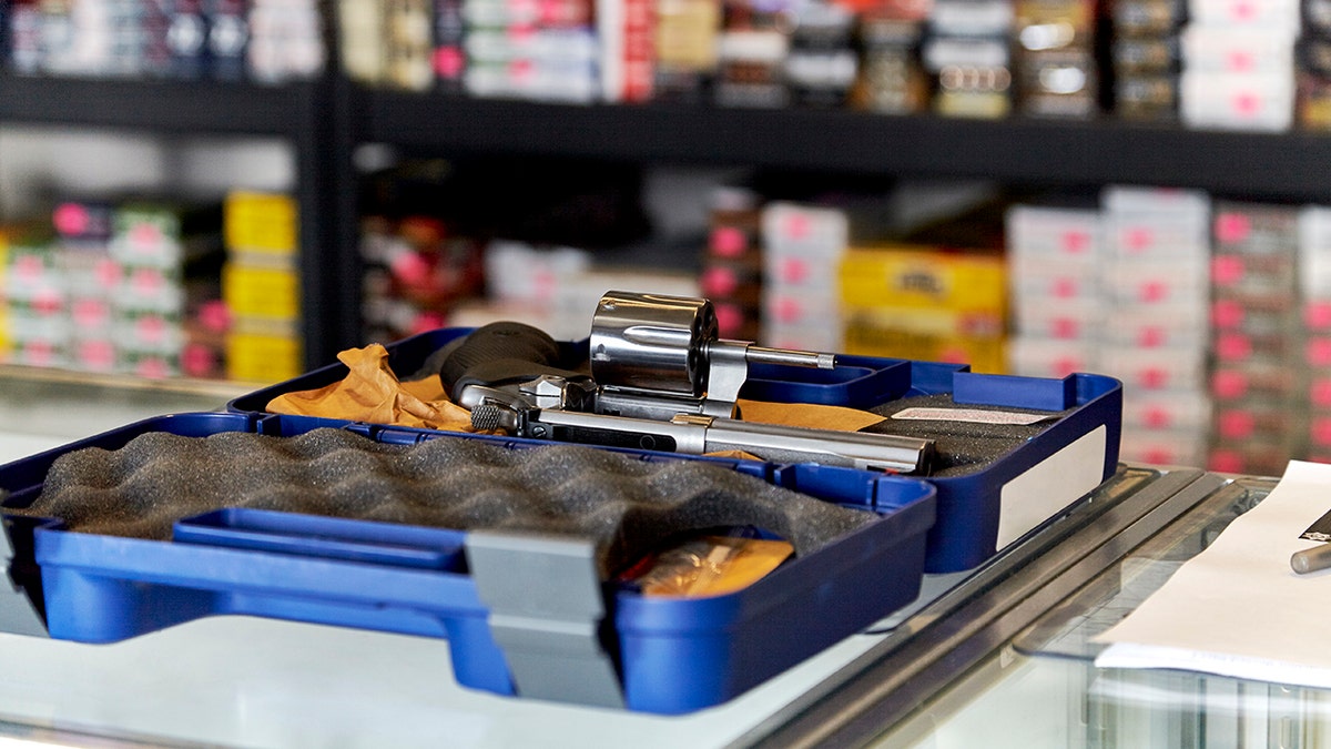 Revolver on a glass showcase displayed in a case with rows of ammunition in the background
