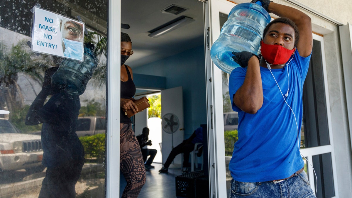 A man carries drinking water for a customer at a water depot store before the arrival of Hurricane Isaias in Freeport, Grand Bahama, Bahamas, Friday, July 31, 2020.