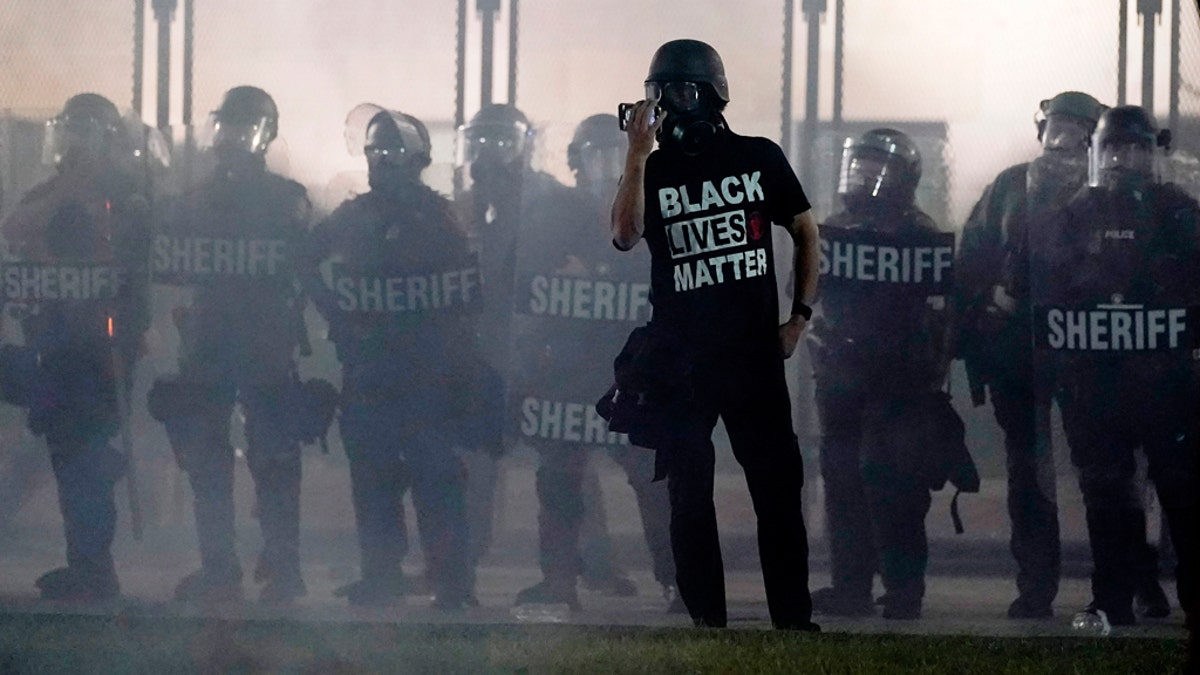 A protester speaks in front of a line of sheriff's deputies in riot gear