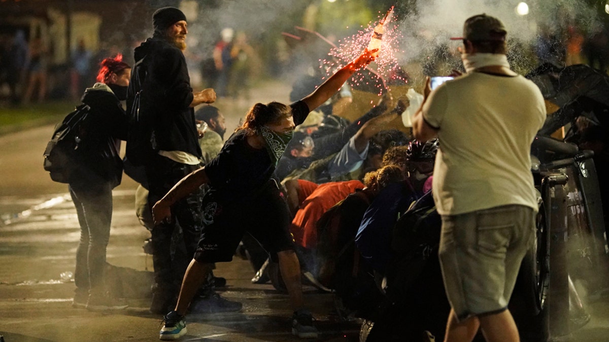 A protester tosses an object toward police during clashes outside the Kenosha County Courthouse late Tuesday, Aug. 25, 2020, in Kenosha, Wis., on third night of unrest following the shooting of a Black man, Jacob Blake, whose attorney said he was paralyzed after being shot multiple times by police. (AP Photo/David Goldman)