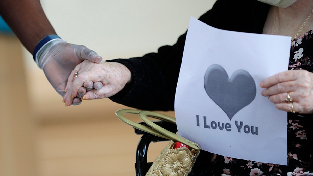 FILE - In this July 17, 2020 file photo, a senior citizen holds the hand of a care coordinator at a Health facility in Miami. One in five U.S. nursing homes say they still faced severe shortages of protective gear like N95 masks this summer, according to a study Thursday that also found facilities struggled with a lack of staff as COVID-19 cases rebounded. (AP Photo/Wilfredo Lee)