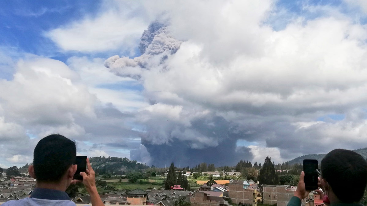 Indonesian men use their mobile phones to take photos as Mount Sinabung spews volcanic materials into the air as it erupts, in Karo, North Sumatra, Indonesia, Monday, Aug. 10, 2020.