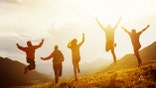 Group of five happy friends is running and jumping in sunset light on background of mountains. Happiness and friendship concept