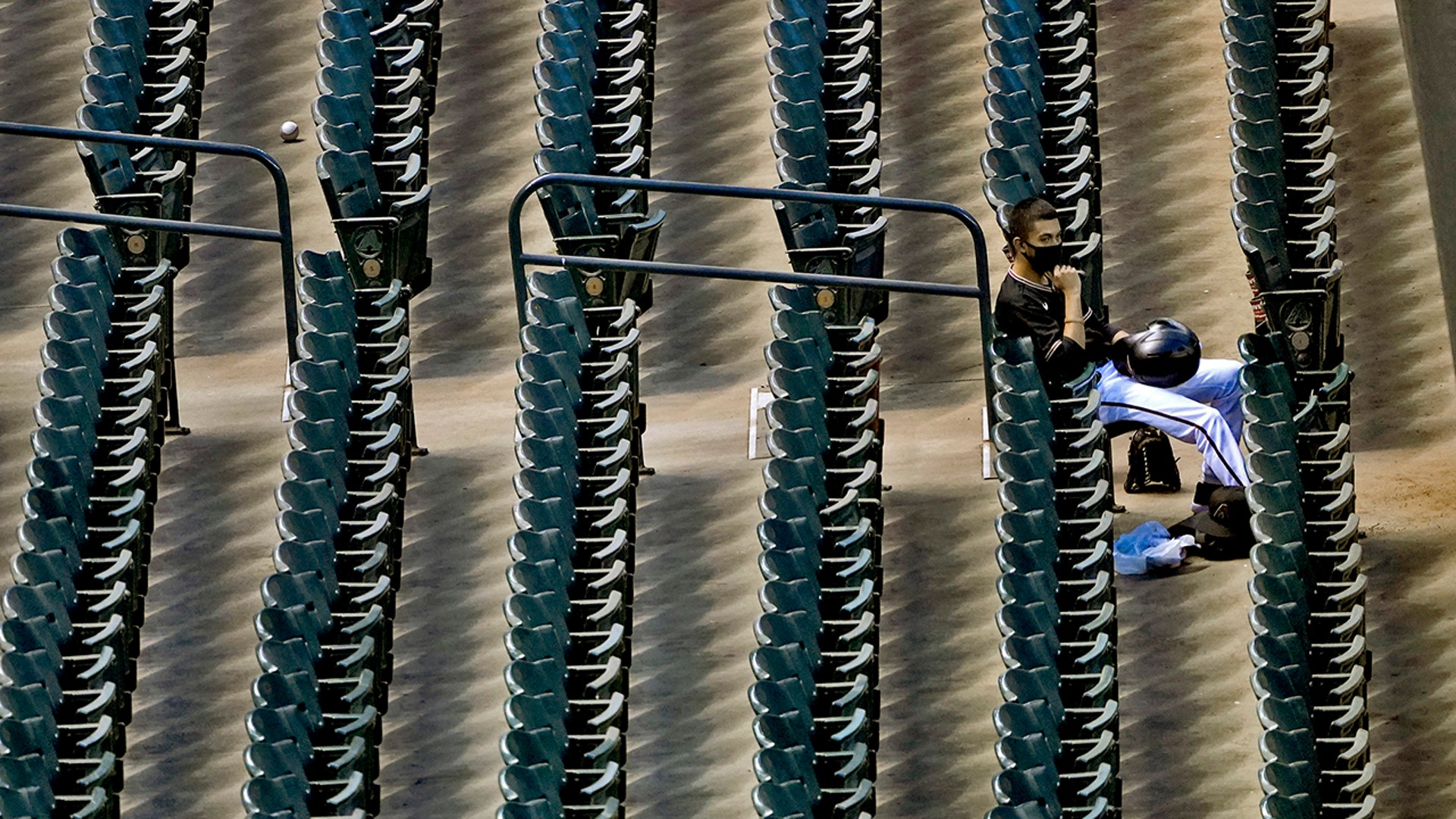 A lone foul ball sits in an aisle as an Arizona Diamondbacks ballboy watches from the stands during a baseball game against the San Diego Padres in Phoenix, Aug. 15, 2020.