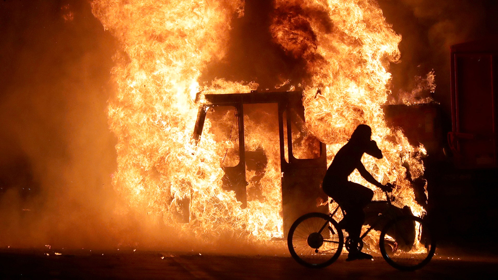 A man on a bike rides past a city truck on fire outside the Kenosha County Courthouse during protests following the police shooting of Jacob Blake in Kenosha, Wis., Aug. 23, 2020. 