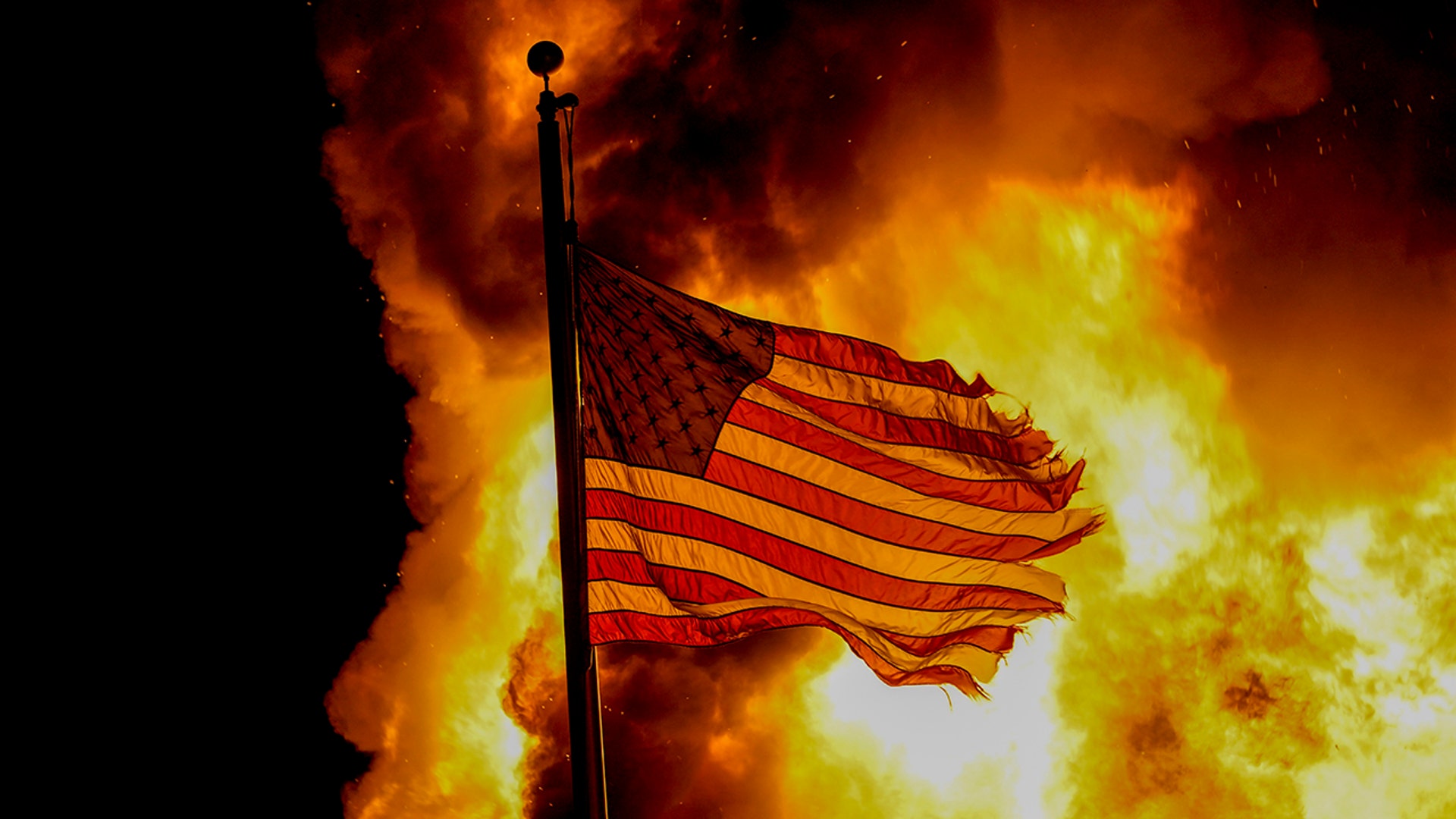A flag flies over a department of corrections building ablaze during protests sparked by the shooting of Jacob Blake by a police officer in Kenosha, Wis., Aug. 24, 2020. 