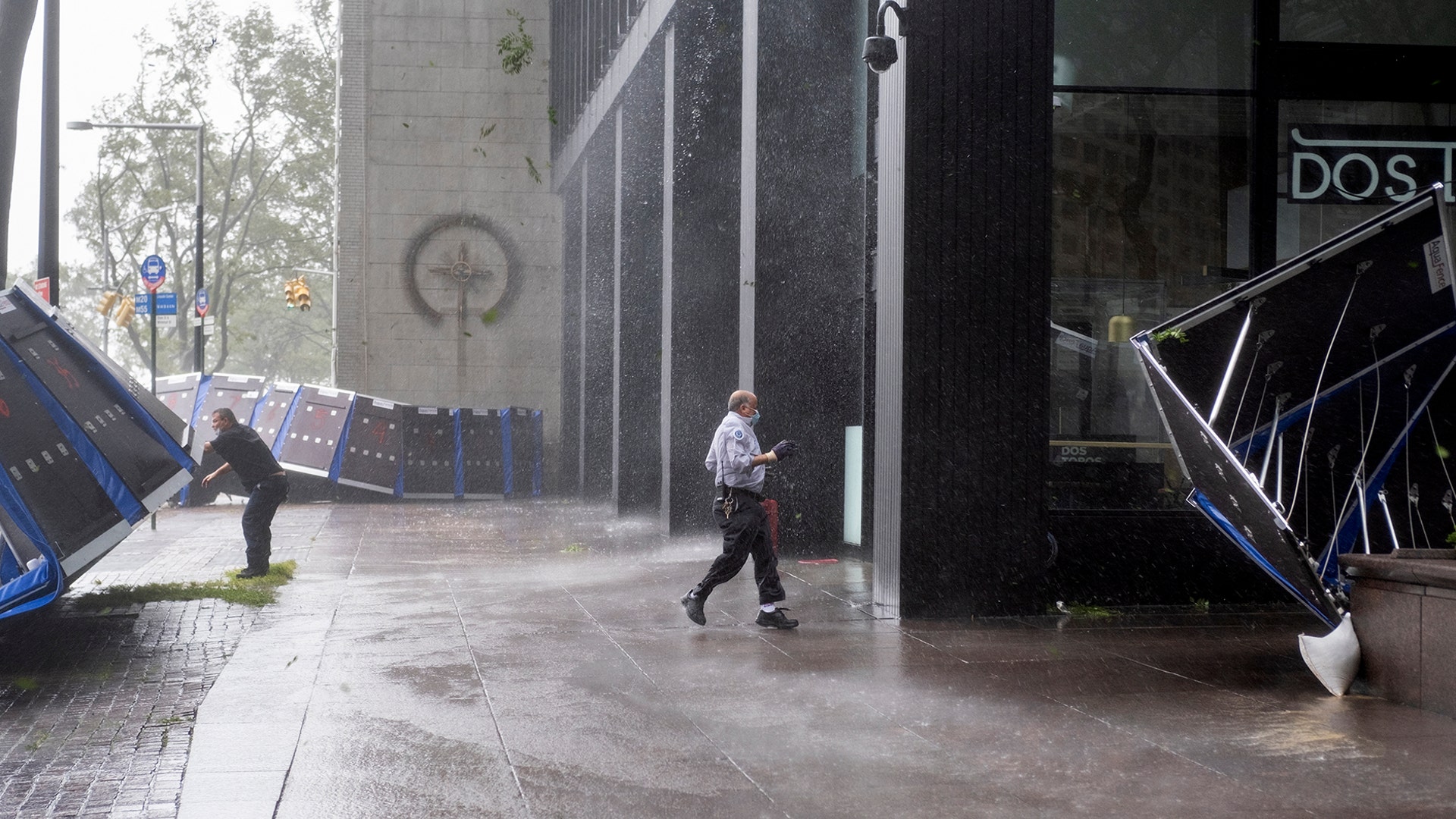 People try to secure barriers meant to block flood waters that were picked up by the wind at a building at Water and State Streets in lower Manhattan Tuesday, Aug 4, 2020, as winds from Tropical Storm Isaias piked them up and tossed them about as the storm moved past, producing strong winds that at times causing damage.