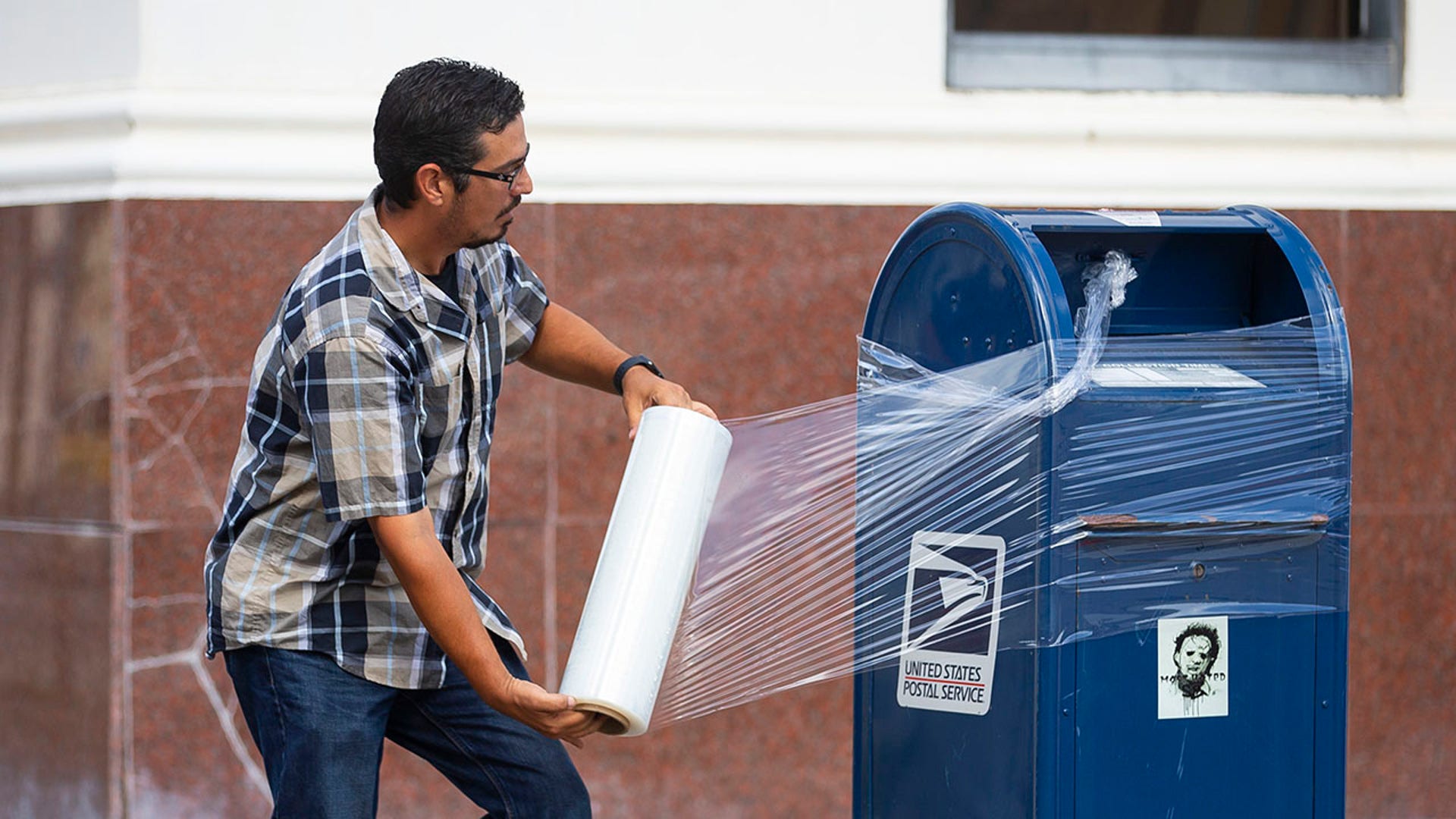 A United State Postal Service Employee covers a mailbox with plastic wrap after removing the last mail from it as the island prepares for possible impact from Hurricane Laura, Tuesday, Aug. 25, 2020, in Galveston. The plastic wrap signals that the final mail has been cleared from the box and prevents people from placing more mail inside in case of flooding. (Mark Mulligan/Houston Chronicle via AP)