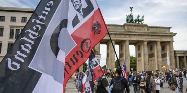 A protester holds a flag featuring a picture of President Trump in front of the Brandenburg Gate before a demonstration against the coronavirus measures by the German Government in Berlin, Germany, Saturday, Aug. 29, 2020. (Christophe Gateau/dpa via AP)