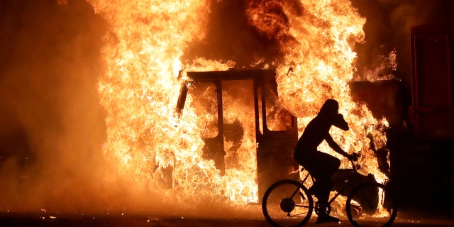 A man on a bike rides past a city truck on fire outside the Kenosha County Courthouse in Kenosha, Wisconsin, U.S., during protests following the police shooting of Black man Jacob Blake August 23, 2020. Picture taken August 23, 2020. Mike De Sisti/Milwaukee Journal Sentinel via USA TODAY via REUTERS MANDATORY CREDIT - RC2DKI99E9P9