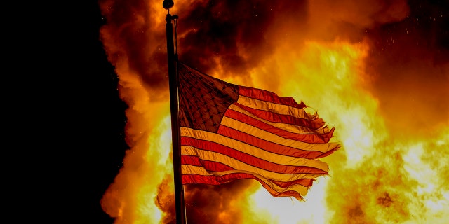 A flag flies over a department of corrections building ablaze during protests, late Monday, Aug. 24, 2020, in Kenosha, Wis., sparked by the shooting of Jacob Blake by a Kenosha Police officer a day earlier. (AP Photo/Morry Gash)