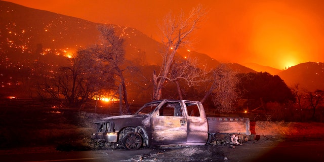 A scorched vehicle rests on Pine Canyon Rd. as the Lake Fire burns a hillside in the Angeles National Forest, Calif., north of Santa Clarita on Thursday, Aug. 13, 2020.