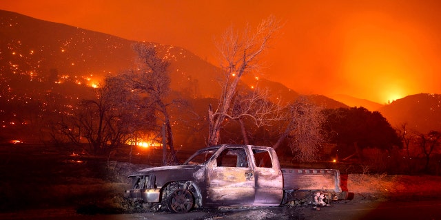 A scorched vehicle rests on Pine Canyon Rd. as the Lake Fire burns a hillside in the Angeles National Forest, Calif., north of Santa Clarita on Thursday, Aug. 13, 2020.